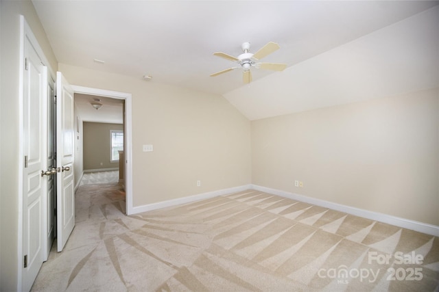 interior space featuring lofted ceiling, ceiling fan, baseboards, and light colored carpet