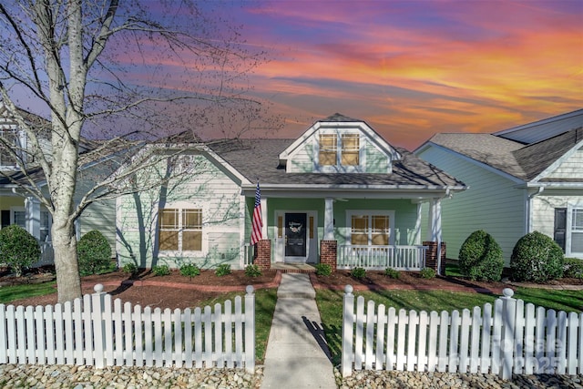 view of front of property with covered porch, a fenced front yard, and brick siding