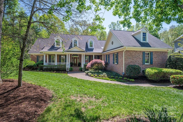 new england style home with brick siding, a porch, a front yard, and a shingled roof