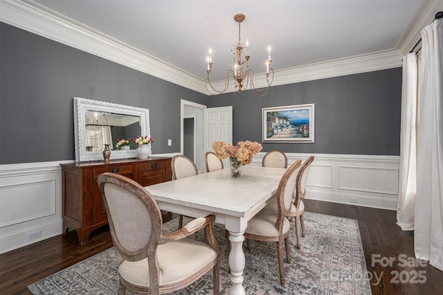 dining room featuring dark wood finished floors, wainscoting, a chandelier, crown molding, and a decorative wall