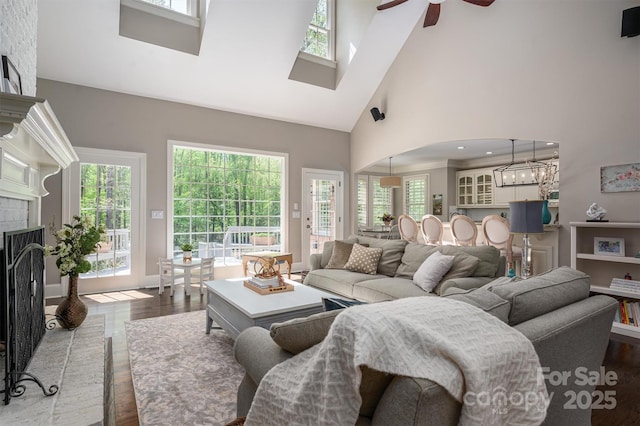 living room featuring plenty of natural light, a high ceiling, wood finished floors, a brick fireplace, and ceiling fan