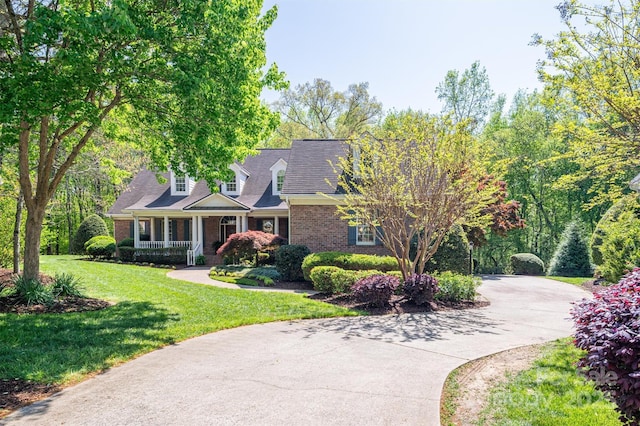 cape cod house with a porch, driveway, brick siding, and a front yard
