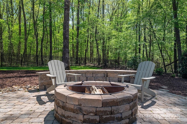 view of patio / terrace featuring a fire pit, a wooded view, and fence