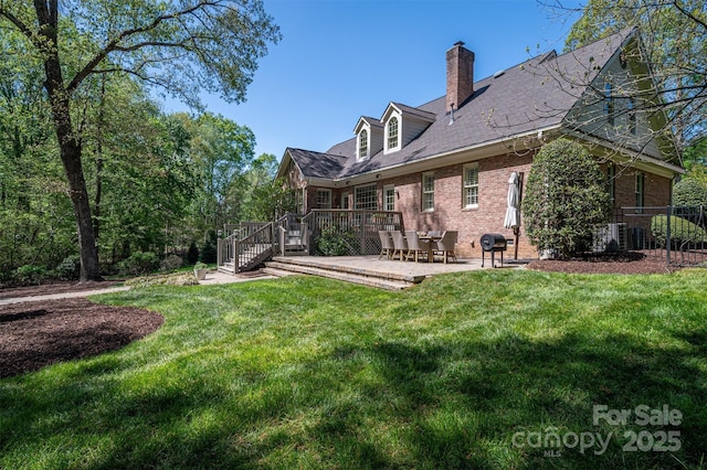 back of house with a chimney, brick siding, a wooden deck, a yard, and a patio