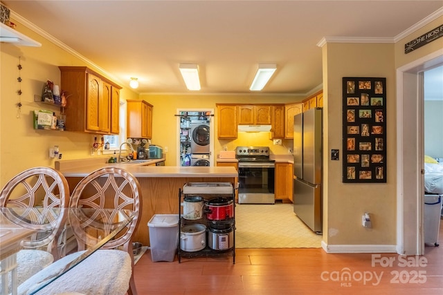 kitchen with stacked washer and dryer, appliances with stainless steel finishes, a sink, a peninsula, and under cabinet range hood