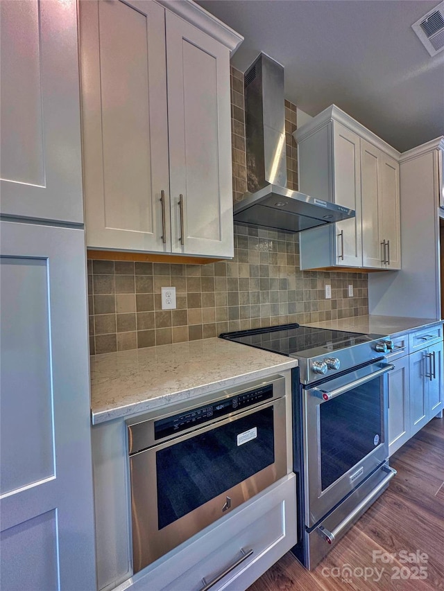 kitchen featuring wall chimney exhaust hood, visible vents, stainless steel appliances, and dark wood-type flooring