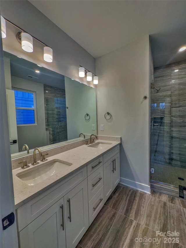 bathroom featuring double vanity, a stall shower, baseboards, and a sink