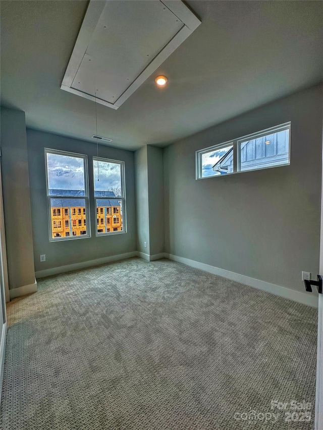 carpeted spare room with attic access and baseboards