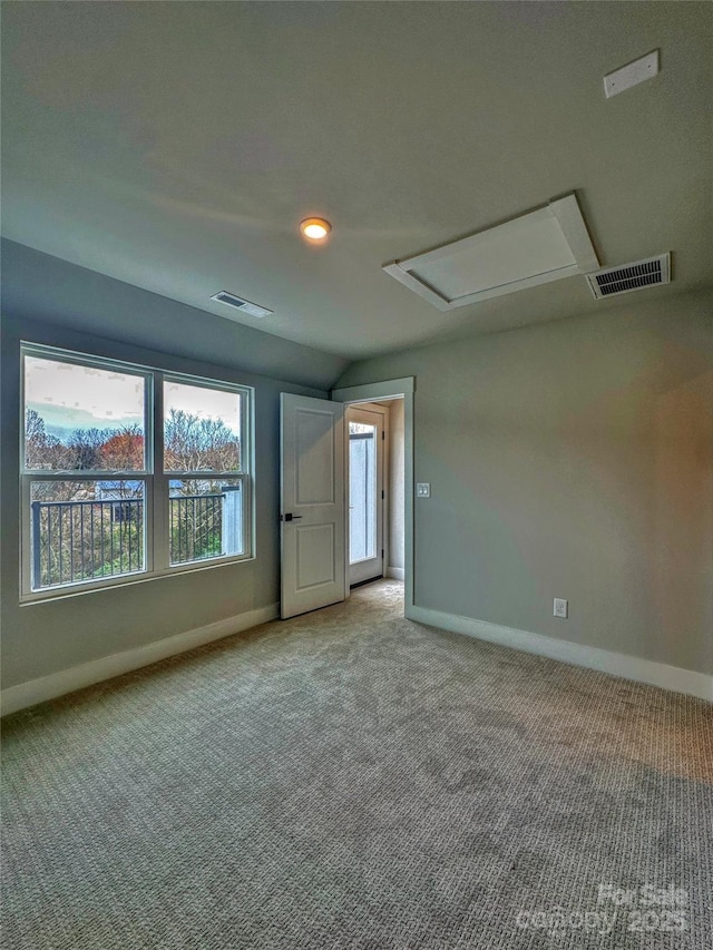 carpeted empty room with baseboards, visible vents, and attic access