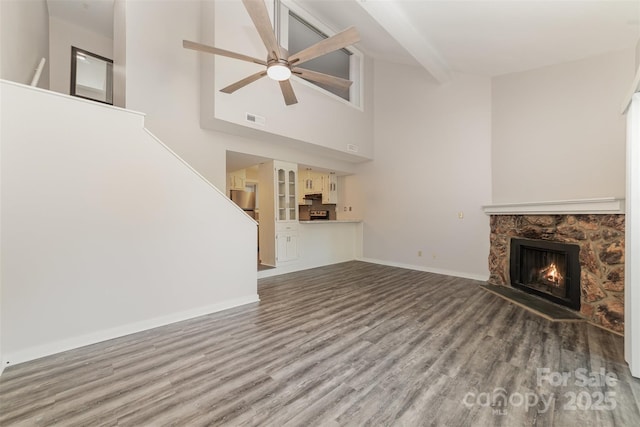 unfurnished living room with beam ceiling, visible vents, a stone fireplace, wood finished floors, and baseboards