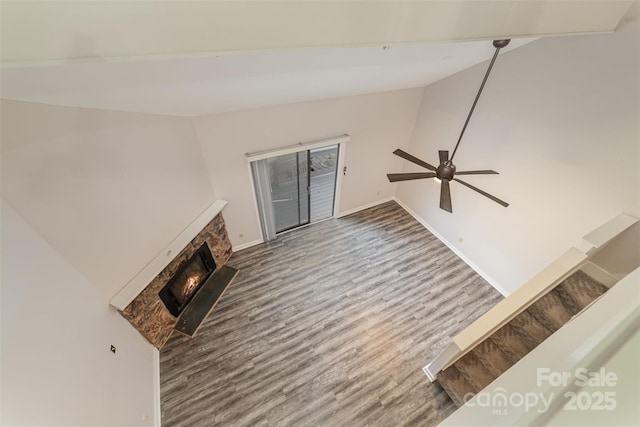 unfurnished living room with wood finished floors, baseboards, vaulted ceiling, a lit fireplace, and stairway