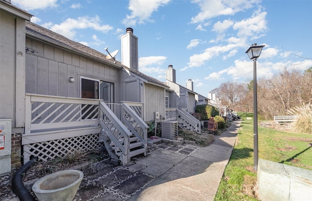 exterior space featuring a yard, a chimney, a wooden deck, and central air condition unit