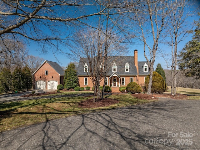 cape cod house with brick siding, a chimney, a garage, driveway, and a front lawn