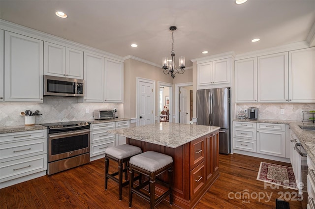 kitchen featuring dark wood finished floors, a kitchen island, appliances with stainless steel finishes, a kitchen bar, and white cabinetry