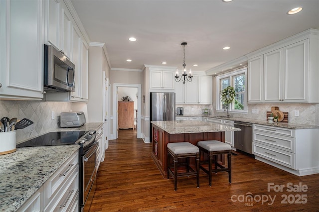 kitchen featuring dark wood-style flooring, a kitchen island, white cabinets, appliances with stainless steel finishes, and crown molding