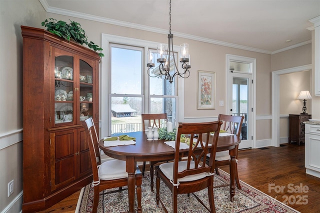 dining space with dark wood-style floors, ornamental molding, and an inviting chandelier