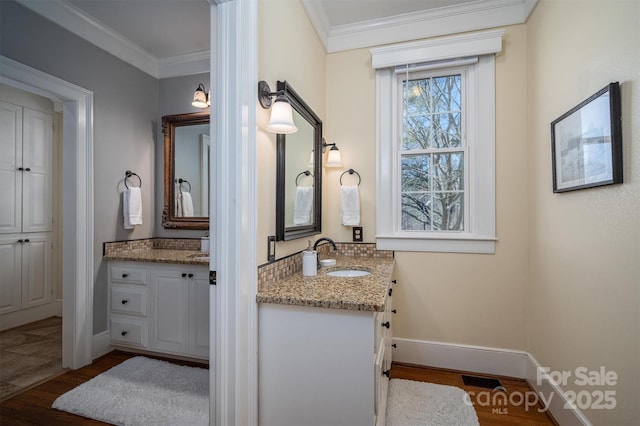 bathroom featuring baseboards, ornamental molding, a sink, and wood finished floors