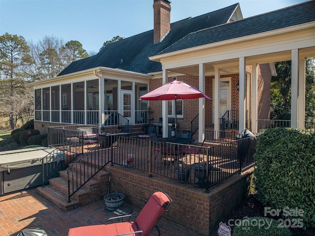 rear view of property with a hot tub, a sunroom, a patio area, and a chimney