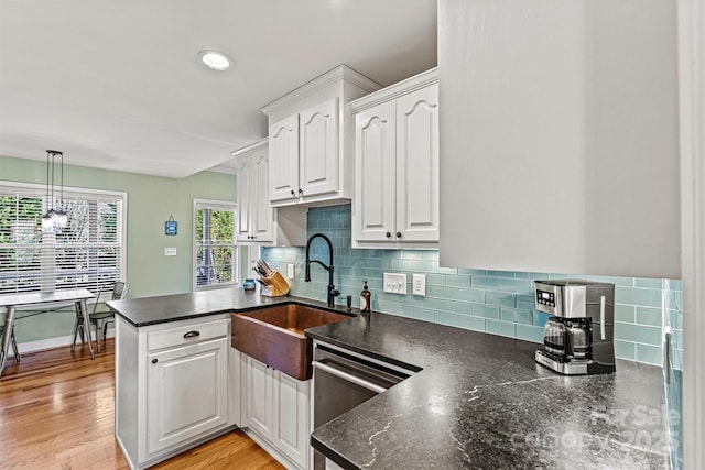 kitchen with dishwashing machine, light wood-type flooring, a peninsula, white cabinetry, and tasteful backsplash