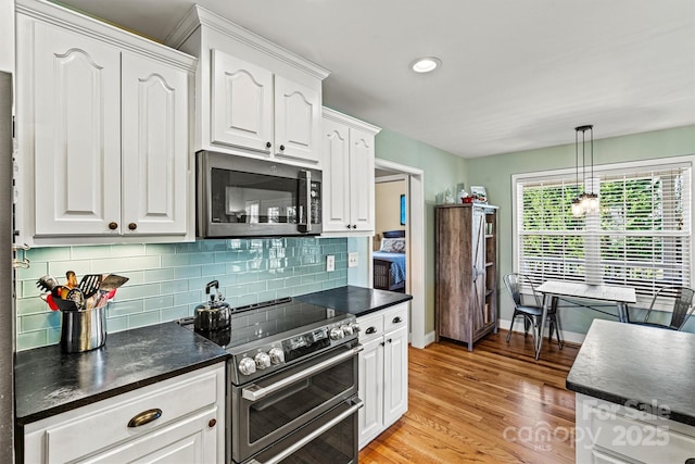 kitchen with light wood-type flooring, tasteful backsplash, dark countertops, stainless steel appliances, and white cabinets