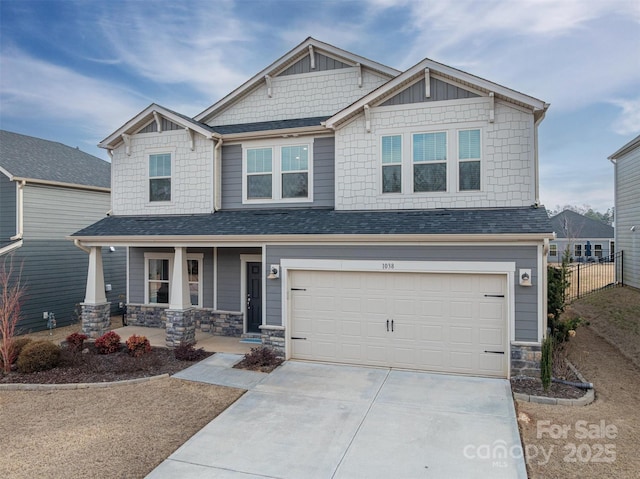 craftsman inspired home featuring concrete driveway, covered porch, fence, a garage, and stone siding