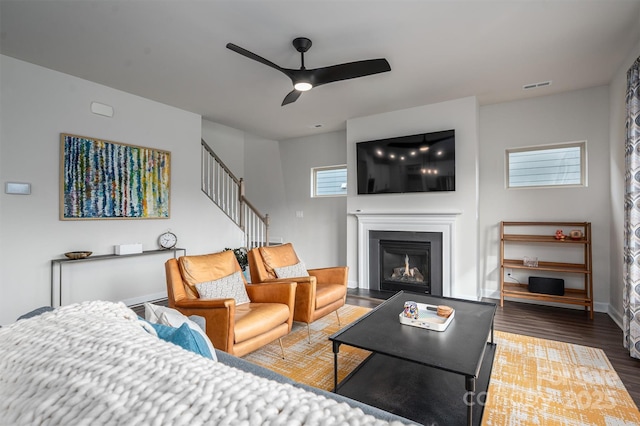 living area featuring visible vents, a fireplace with raised hearth, ceiling fan, stairway, and wood finished floors