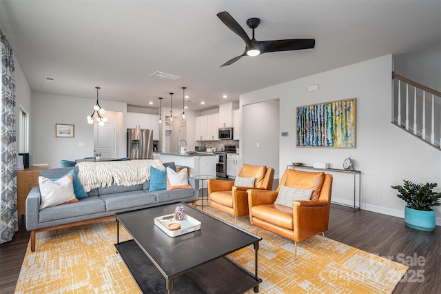 living room with ceiling fan, wood finished floors, visible vents, baseboards, and stairs