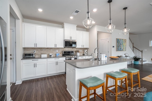 kitchen with dark wood finished floors, stainless steel appliances, decorative backsplash, a sink, and a kitchen breakfast bar