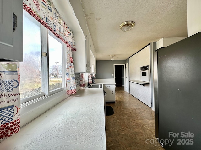 kitchen featuring a textured ceiling, dark floors, oven, a sink, and light countertops