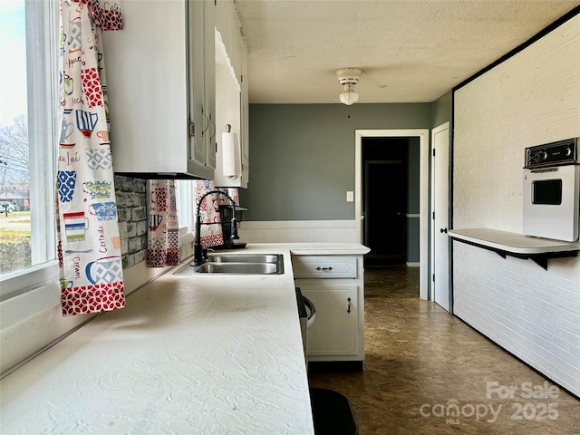 kitchen featuring white oven, light countertops, wainscoting, a sink, and a textured ceiling