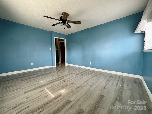 unfurnished room with ceiling fan, a textured ceiling, wood finished floors, and baseboards