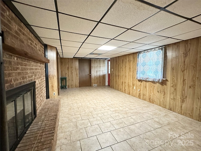 below grade area featuring wood walls, a fireplace, and a paneled ceiling