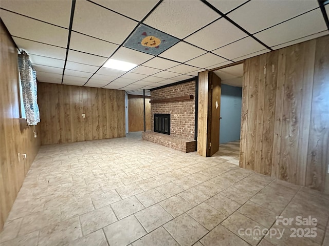 finished basement featuring wood walls, a brick fireplace, and a paneled ceiling