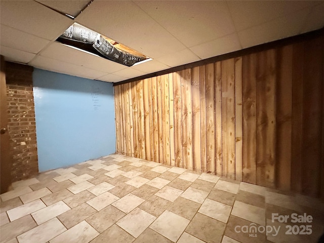 finished basement featuring a drop ceiling and wooden walls