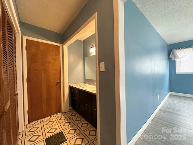 corridor featuring a textured ceiling, light floors, a sink, and baseboards