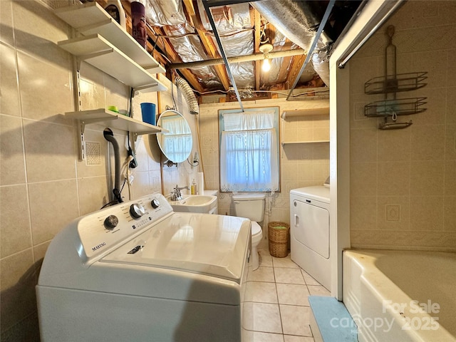 clothes washing area with a sink, laundry area, washing machine and clothes dryer, and tile walls