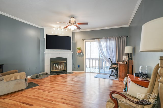 living room featuring ceiling fan, wood finished floors, a fireplace with flush hearth, and crown molding