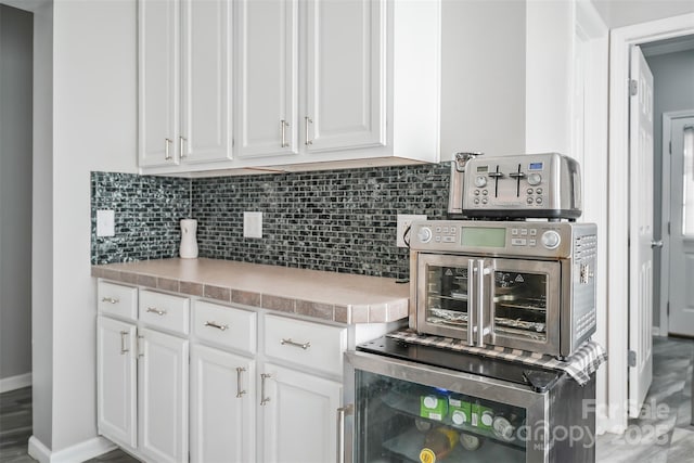 kitchen featuring light countertops, decorative backsplash, white cabinets, beverage cooler, and baseboards