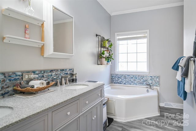 bathroom with a garden tub, double vanity, visible vents, ornamental molding, and wood finished floors