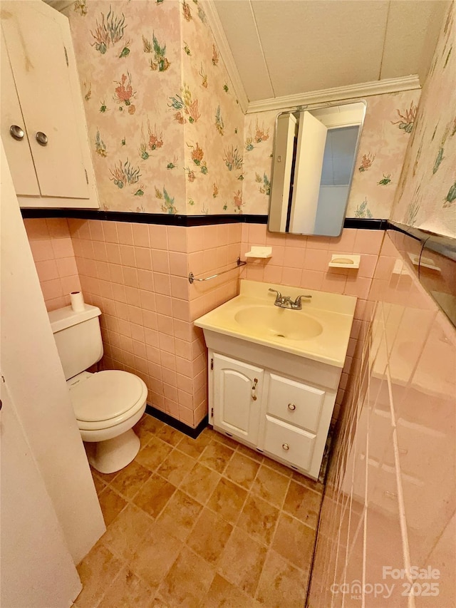 bathroom with a wainscoted wall, vanity, toilet, and wallpapered walls