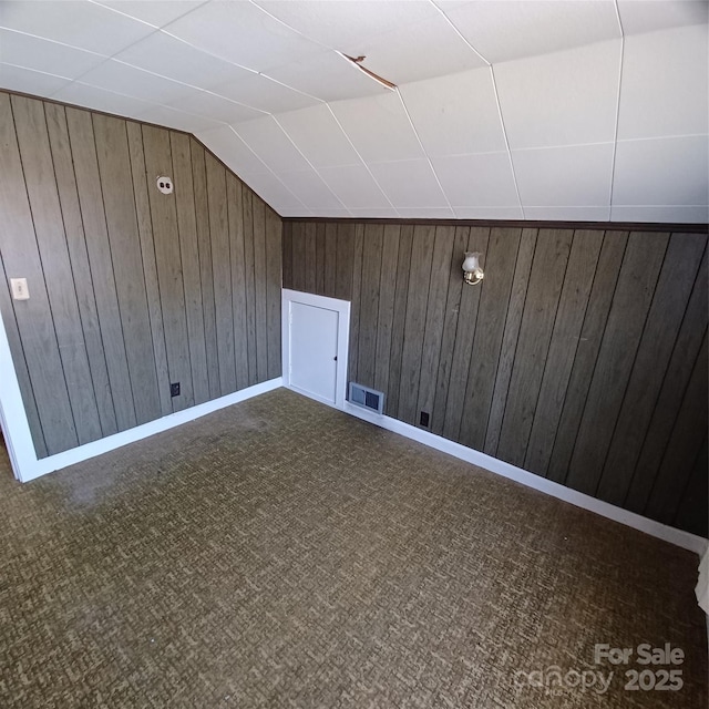 bonus room with lofted ceiling, wood walls, dark carpet, and visible vents