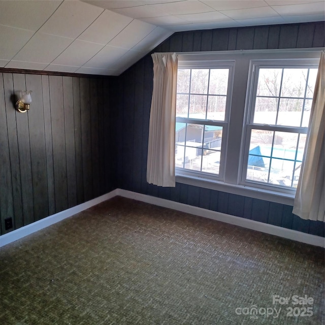 additional living space with lofted ceiling, dark carpet, wooden walls, and baseboards