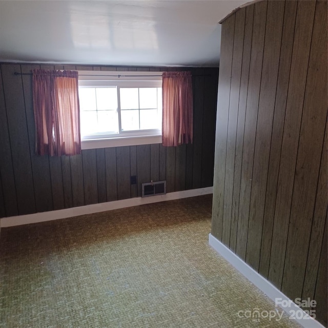 empty room with wood walls, carpet, visible vents, and baseboards