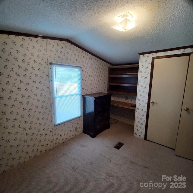 unfurnished bedroom featuring wallpapered walls, ornamental molding, vaulted ceiling, a textured ceiling, and carpet floors