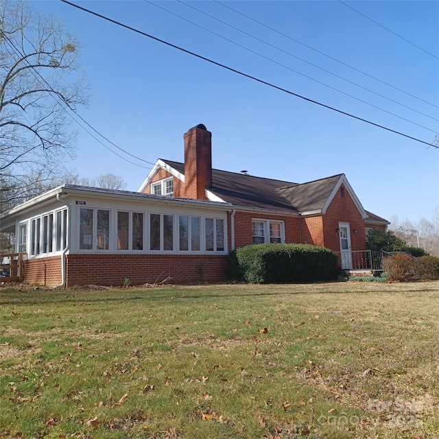 rear view of house with a sunroom, a chimney, a lawn, and brick siding