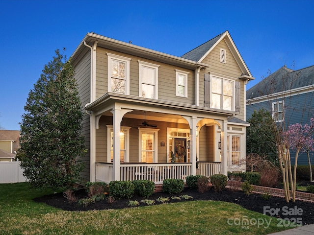 traditional-style home featuring covered porch, fence, and a front lawn