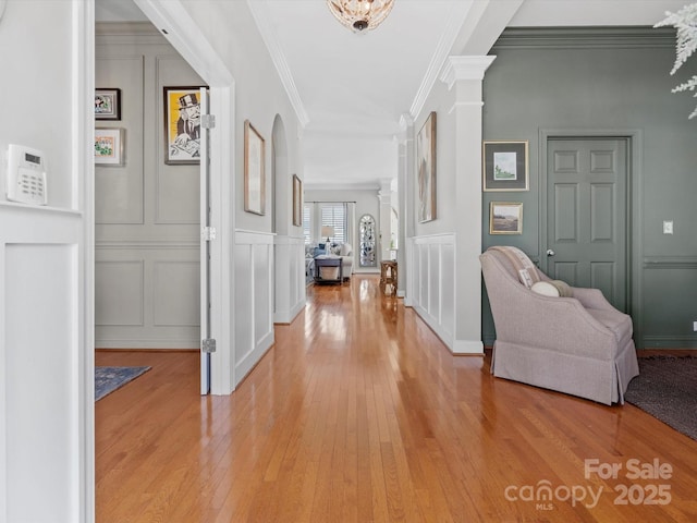 hall featuring ornate columns, crown molding, light wood-type flooring, and a decorative wall