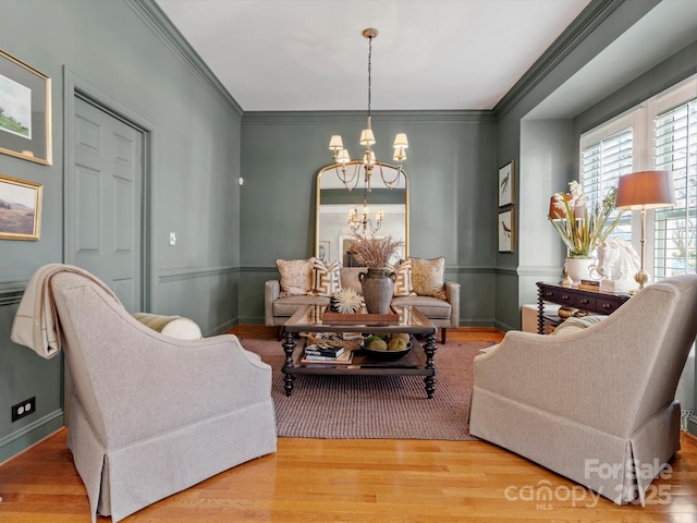 living area with baseboards, ornamental molding, wood finished floors, and an inviting chandelier