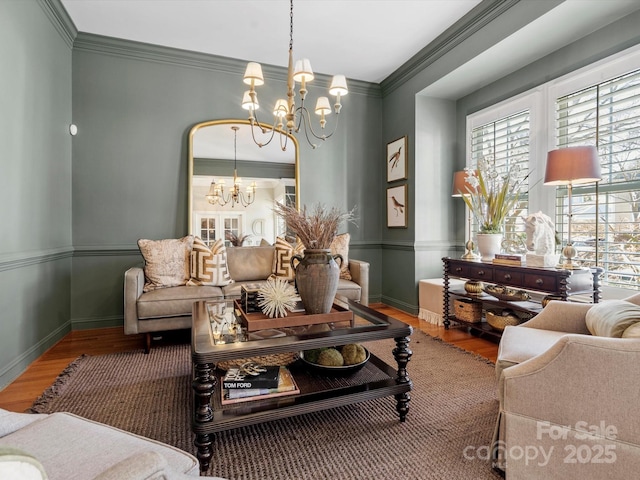 living area featuring crown molding, baseboards, wood finished floors, and a notable chandelier