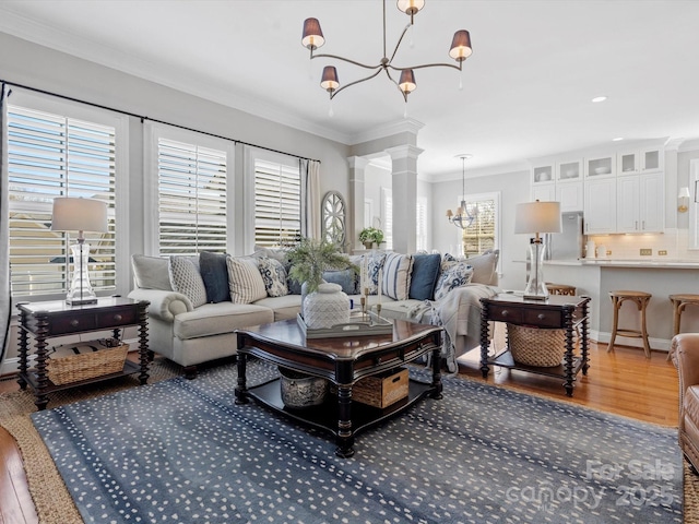 living area with a chandelier, wood finished floors, crown molding, and decorative columns